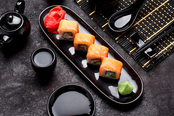 Japanese cuisne. Salmon sushi roll (philadelphia) on a black plate and dark concrete background.