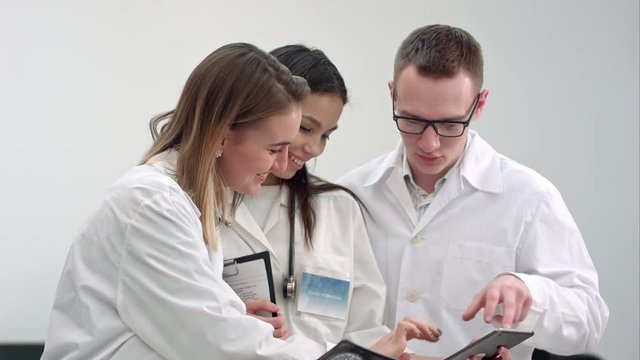Three smiling doctors discussing X-ray while using tablet