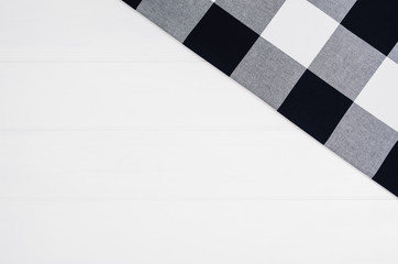 Top view of black checkered napkin or tablecloth on white wooden table with visible planks, texture and copy space for text.