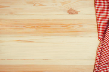 Top view of red checkered napkin or tablecloth on raw wooden table with visible planks, texture and copy space for text.