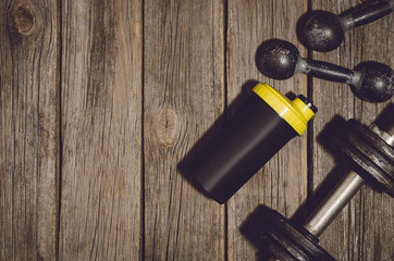 Old iron dumbbells or exercise weights and protein shaker bottle outdoor on an old wooden deck,...
