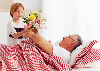 young grandson with flower bouquet came to visit his sick grandpa in hospital ward