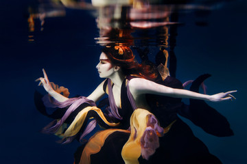 girl in colorful clothes on the dark background swimming underwater