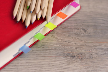 Obraz premium Red diary notebook and colored pencils on the desk wood texture.