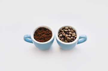 two blue macro coffee espresso cups with the fresh coffee beans and with a ground coffee on the white background