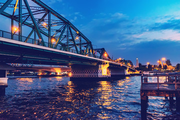 Phra Pokklao Bridge closeup over Chao Phraya River at night with lights and reflections, Bangkok, Thailand. Soft focus.