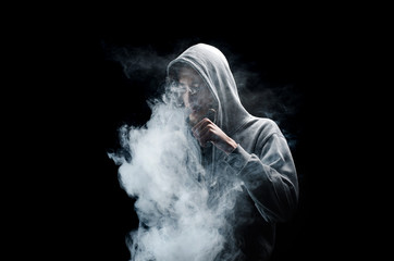 One man in the hood vaping e-cigarette and blowing a cloud.