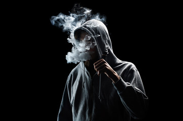 One man in the hood vaping e-cigarette and blowing a cloud. - obrazy, fototapety, plakaty