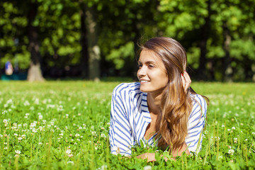 Fototapeta premium Attractive young brunette woman lying on green grass field at su