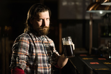 brutal hipster bearded man in a plaid shirt is holding a glass of beer