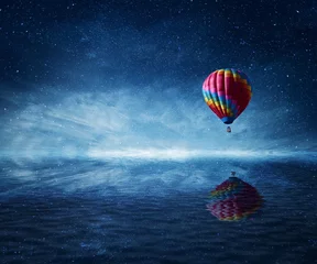 Schilderijen op glas Heteluchtballon die over de koude donkerblauwe zee vliegt. Prachtig landschap met een sterrenhemel achtergrond en water reflectie. © psychoshadow