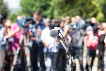 Press conference. Microphone in focus, blurred camera operators and reporters in background.