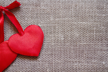 two red satin hearts lie together on a linen background