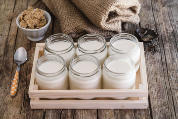 Homemade yogurt in glass jar and wooden box. Antique wooden table. Burlap and cereal bowl on...