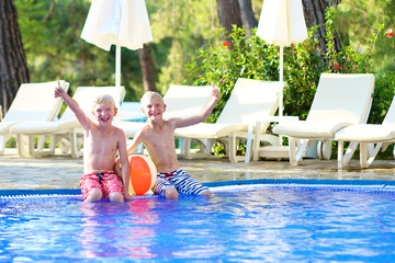 Two happy boys, laughing teenage twin brother, enjoying sunny summer vacation playing with inflatable ball in outdoors swimming pool