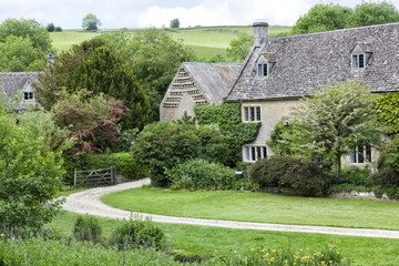 Rural Cotswolds village with old, traditional stone homes in green valley, on a summer day