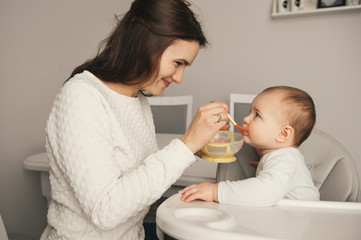 Mom feeding her baby girl with a spoon. Mother giving food to her eight-month child at home. Baby...