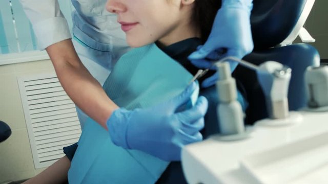 Assistant clings handkerchief on woman in dentist chair in cabinet. Nice female with brown picked hair sitting in profile, ready for treatment. Cute client waiting for curing. Pleasant blonde