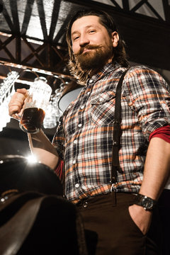 hipster bearded man in a plaid shirt is holding a glass of beer