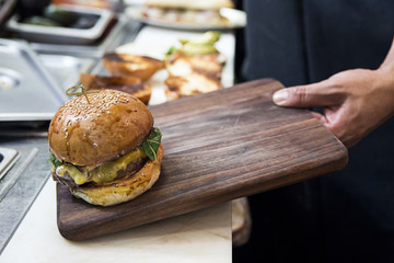 A cook puts a cheesburger on a cutting board to be cut and served.