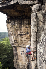 A young white man leads a traditional rock climb in the New River Gorge of West Virginia.