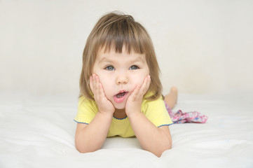 Funny little girl make face massage with cute cheeks lying on bed isolated, having fun and grimacing