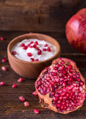 Sliced red pomegranate on wooden desk with yogurt in behind.
