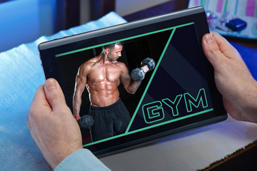 man at home searching information in internet in gym website for training / hands of a man with tablet at home on page web with an announcement advertising of the Gym