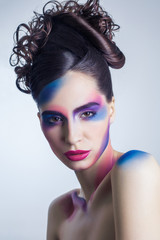 beautiful young woman with creative colored makeup and curly collected hairstyle and painted colored body. 
