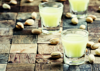 Pistachio liqueur in glass and nuts, vintage wooden background,