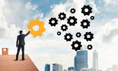 Businessman standing with back on house brick roof and drawing. 