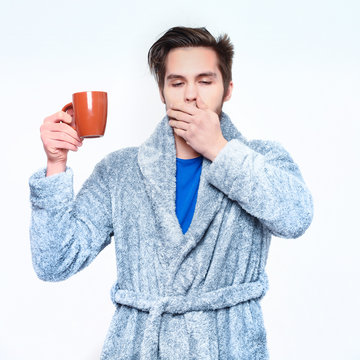 handsome bearded yawning sleepy man with cup in terry bathrobe