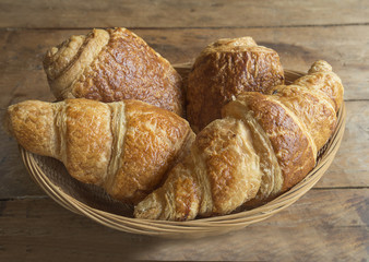 wicker basket with french croissants on rustic wooden background