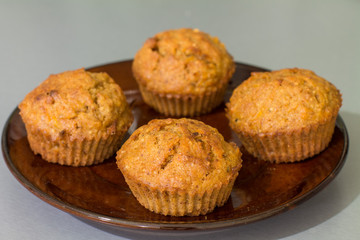 Four muffins with carrot, walnut and cinnamon in ceramic plate on gray kitchen table. 