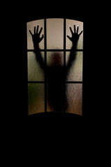 Silhouette of an unknown man  with his hand on a door through a closed glass door