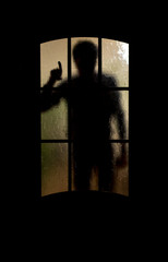 Silhouette of an unknown man shows the index finger through a closed glass door