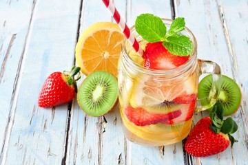 Lemon, strawberry, kiwi detox water in a mason jar glass with scattered fruit against a rustic blue wood background