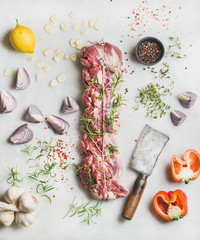 Raw uncooked roast beef meat cut with herbs, vegetables and spices over light grey marble background, top view
