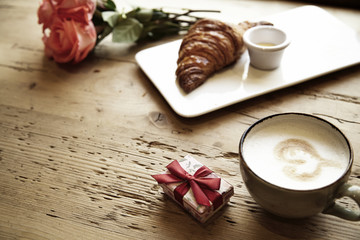 Fresh bakery croissant, coffee with heart sign, rose flowers on wooden table. Romantic breakfast for Valentine's Day celebrate concept. Focus on box