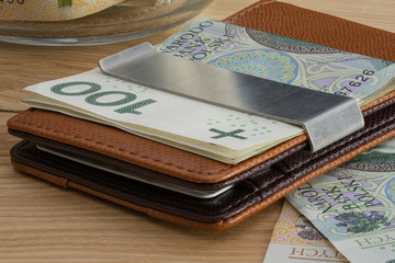 cienki portfel z polskimi banknotami i kartami płatniczymi na ceglanym tle