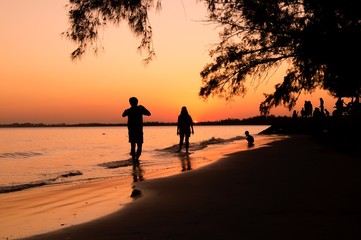 Silhouette of man taking picture his girlfriend on the beach at sunset