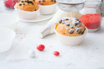 Vanilla cupcakes with chocolate chips and whipped cream in pastry bag sprinkled with powdered sugar on the white background