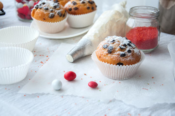 Vanilla cupcakes with chocolate chips and whipped cream in pastry bag sprinkled with powdered sugar on the white background