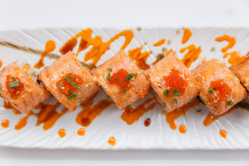 Torched Salmon Maki Sushi with Shrimp Tempura, Avocado and Cheese inside. Topping with Sauce, Ebiko (Shrimp Egg) and Scallion.