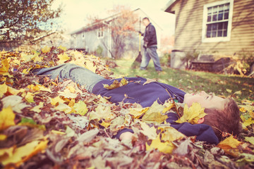 Young boy daydreaming in a pile of fall leaves while his father