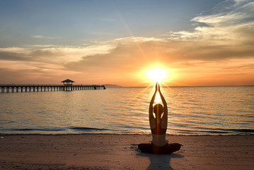 young woman yoga practice on the beach at sunset