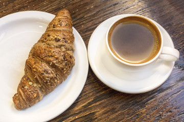 Cup of dark coffee with cereal croissant