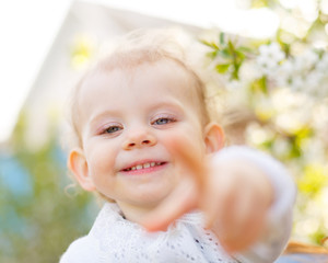 Cute little girl shows the index finger at the camera. Spring mood. Soft focus.