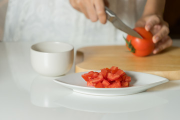 Woman is hands cutting tomato on wood board.
