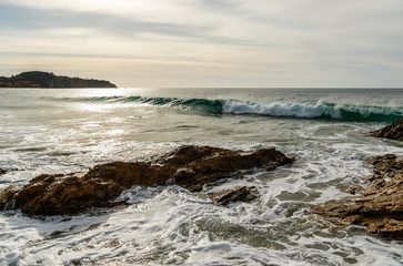 Fototapeta na wymiar Waves of the calm Pacific Ocean gently break just beyond a rocky section of shoreline at Crystal Cove State Park in Laguna Beach, California. 